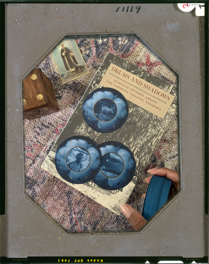 inside a vintage gray frame, an image of a brown hand holding a deck of blue circular playing cards. three cards lay upright on top of a book that’s on top of a rug, surrounded by Black spiritual paraphernalia.