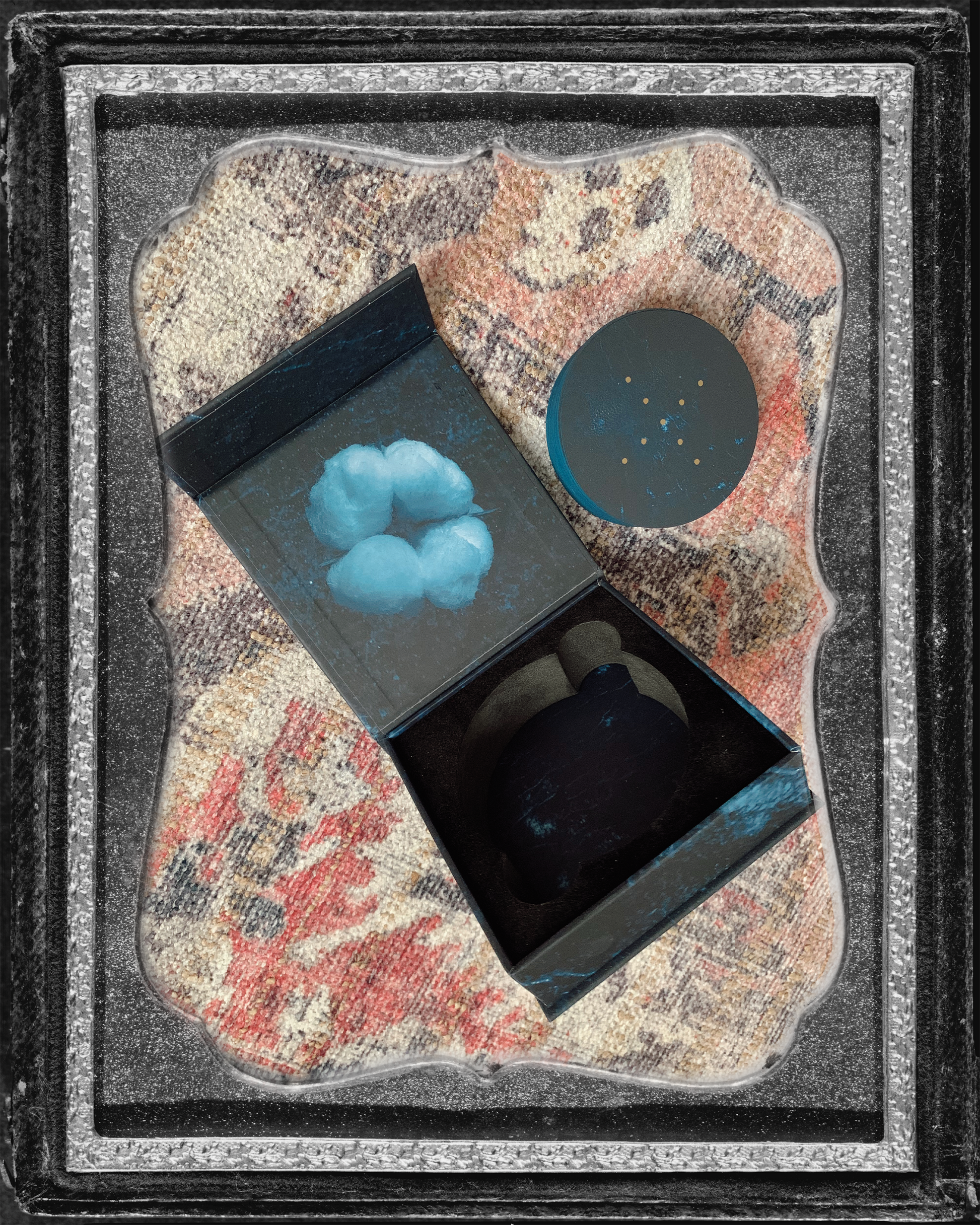 inside a vintage silver frame is a photo of the interior of the square box for Grandma Baby's 52 Blues, next to a pile of cards, on a colorful flat weave carpet.